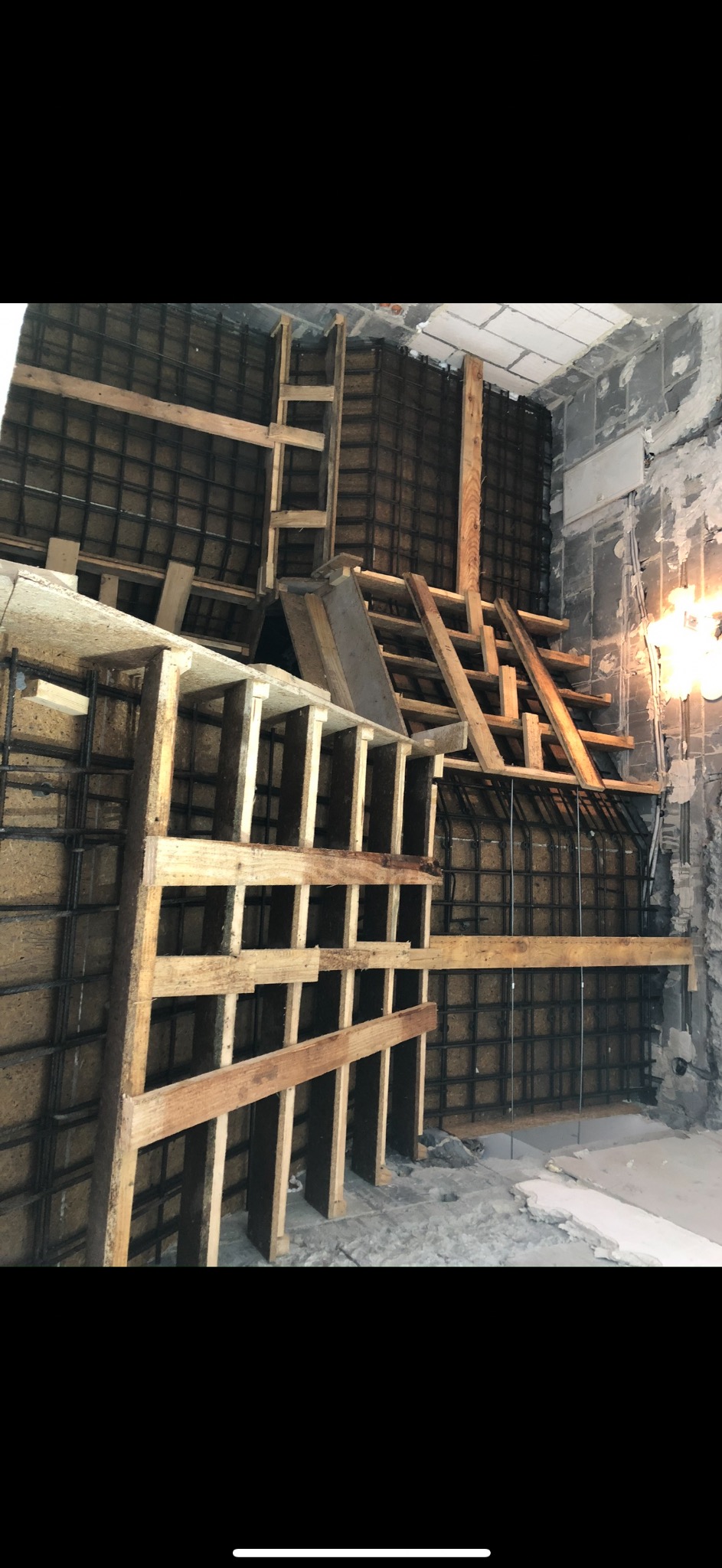 Wnętrze w trakcie remontu: szalunek z drewnianych belek i siatki zbrojeniowej na ścianach. Widoczne surowe ściany i podłoga w trakcie przygotowania do dalszych prac.