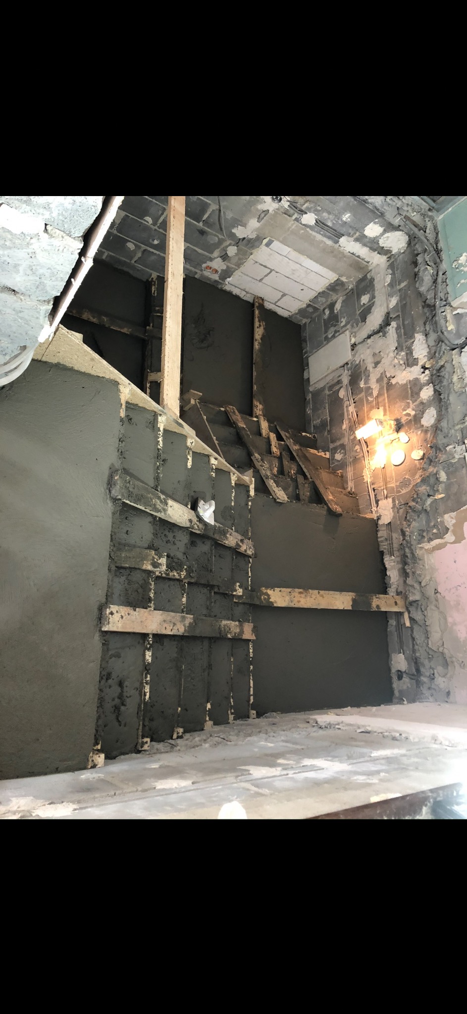 Ściana w trakcie wyrównywania zaprawą, z widocznymi drewnianymi elementami konstrukcyjnymi. Surowy stan wnętrza, widoczne instalacje i fragmenty starego wykończenia.