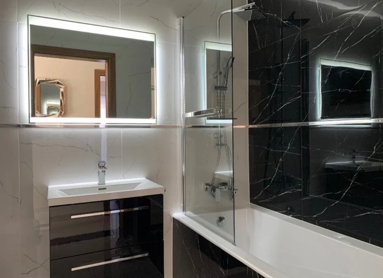 Nowoczesna łazienka z czarno-białymi marmurkowymi płytkami, podświetlanym lustrem i kabiną prysznicową z przezroczystego szkła. Minimalistyczny design.