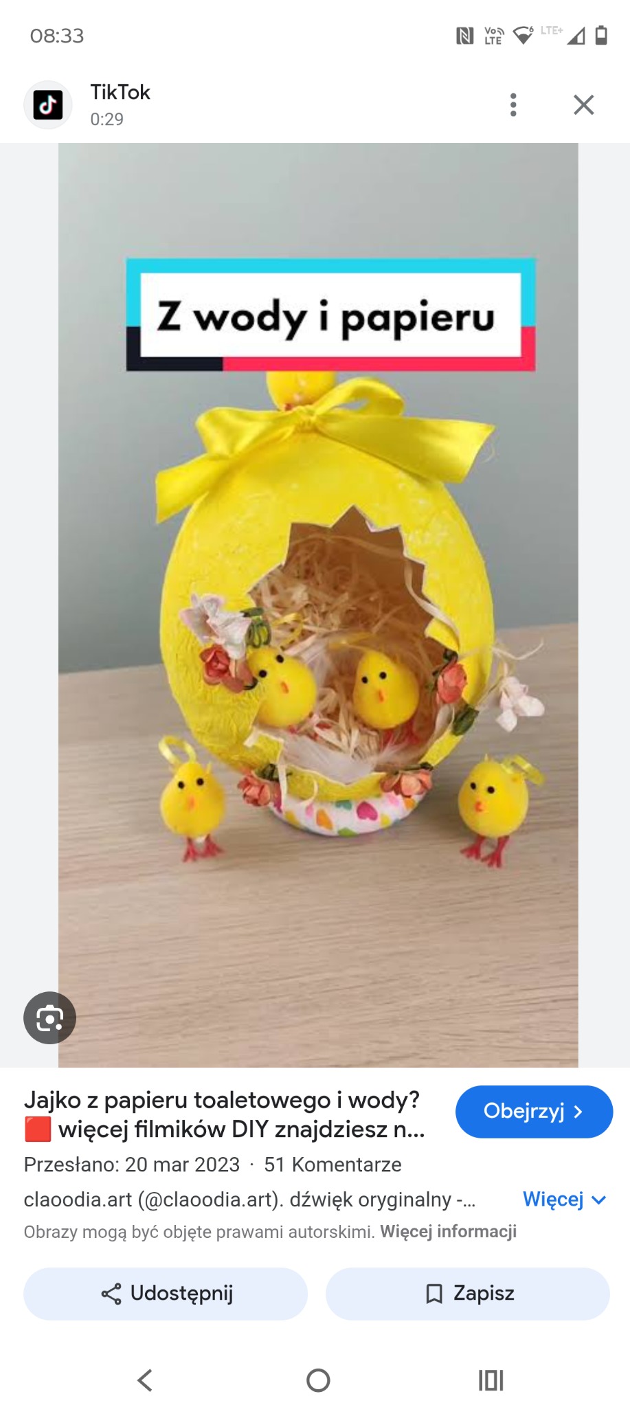 Żółte, dekoracyjne jajo wielkanocne z papieru i wody, ozdobione kokardą i pisklętami, na jasnym tle. Rękodzieło DIY.