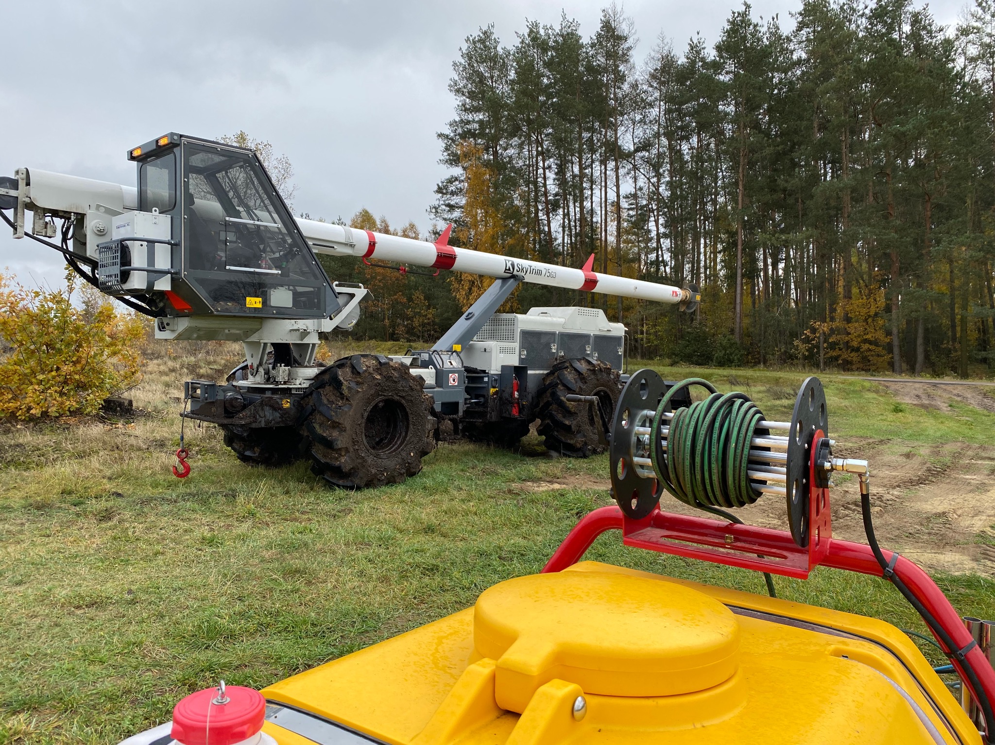 Specjalistyczna maszyna Sky Trim 7563 do pielęgnacji drzew w Łomży, z wysięgnikiem i kołami terenowymi, na tle lasu. Widoczny fragment żółtego zbiornika.