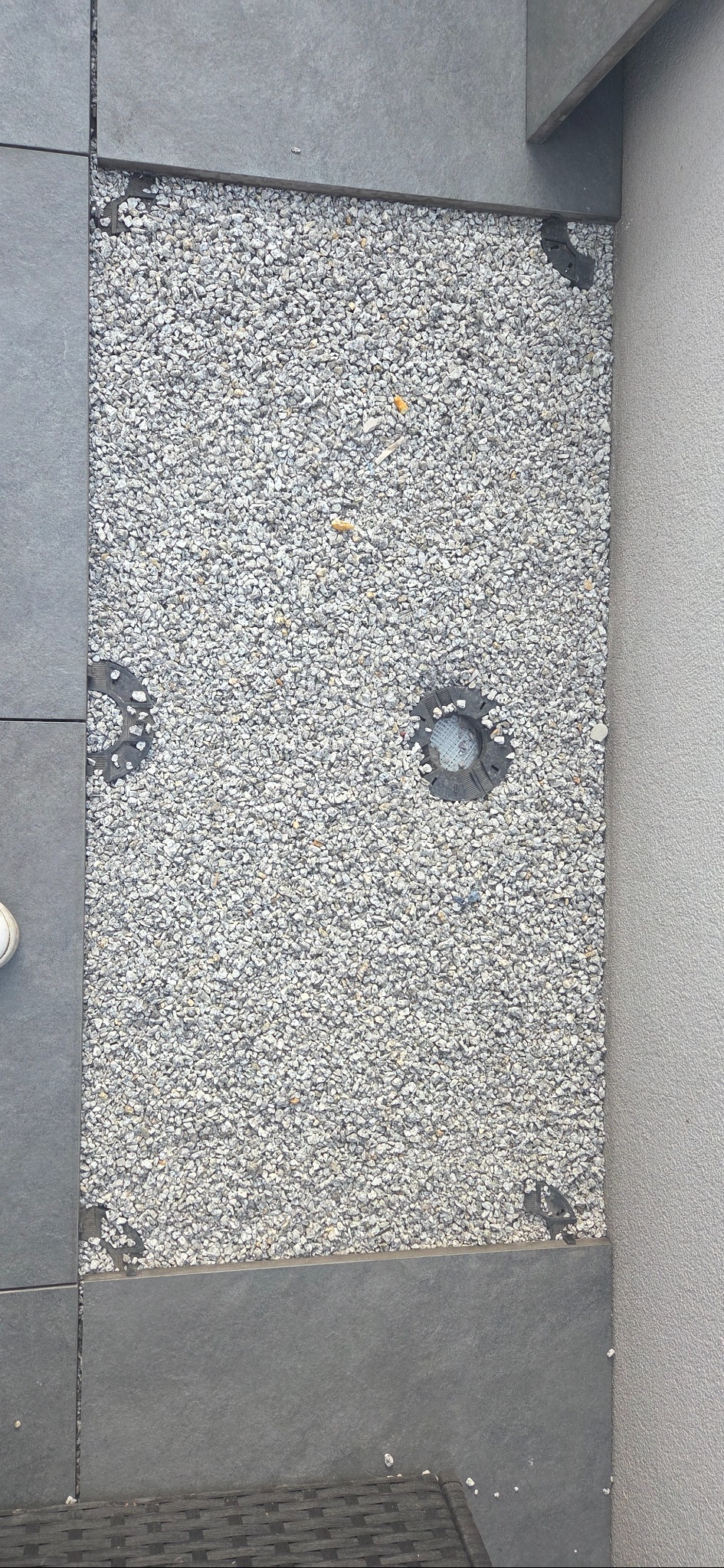 Wykończona powierzchnia z szarych płytek i białego żwiru, z wbudowanymi punktami oświetleniowymi. Widok z góry, ukazujący detale materiałów i precyzję wykonania.