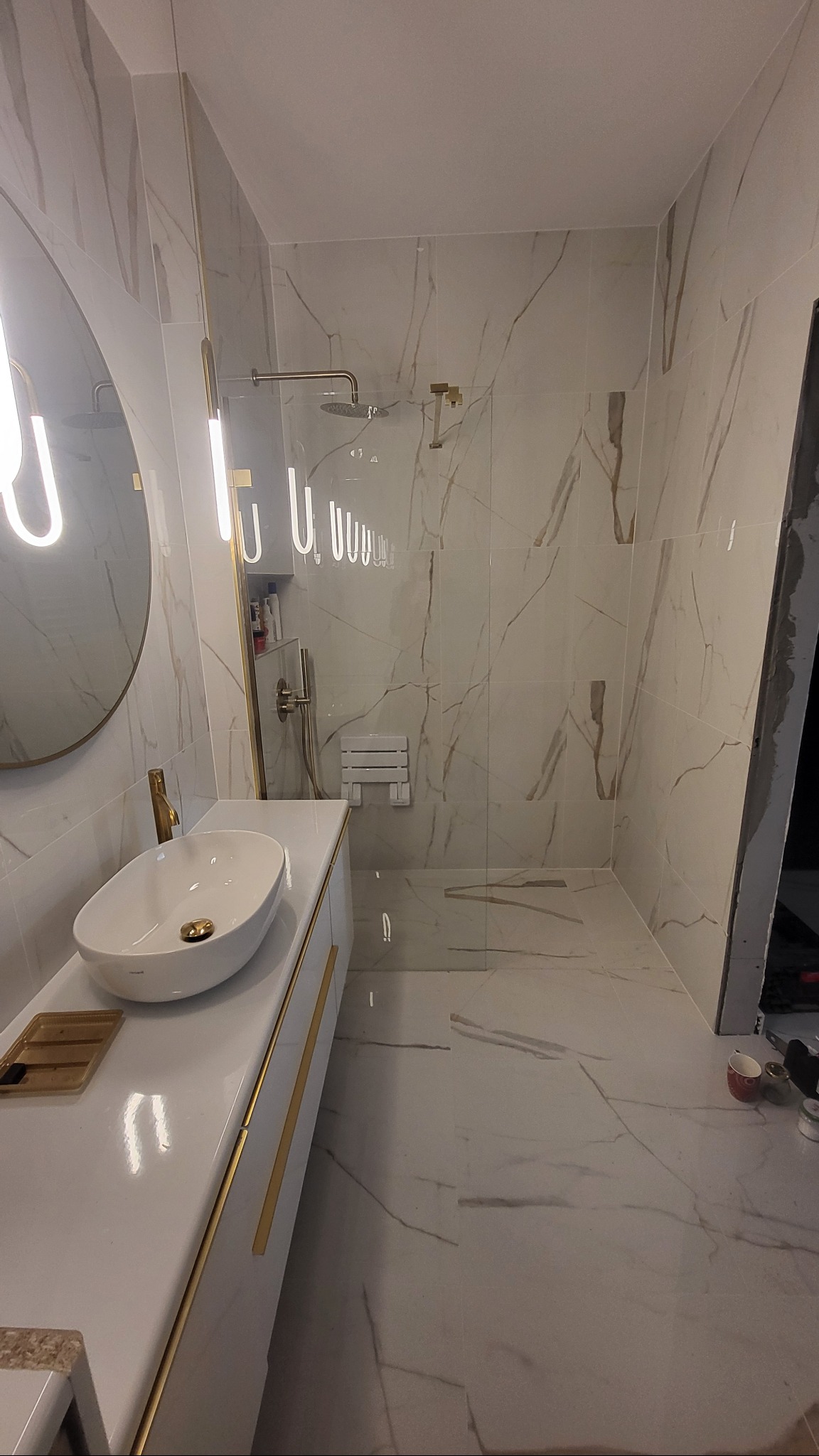 Elegancka łazienka w bieli i złocie: umywalka nablatowa, kabina walk-in z deszczownicą, marmurowe płytki i oświetlenie LED. Nowoczesny design z dbałością o detale.