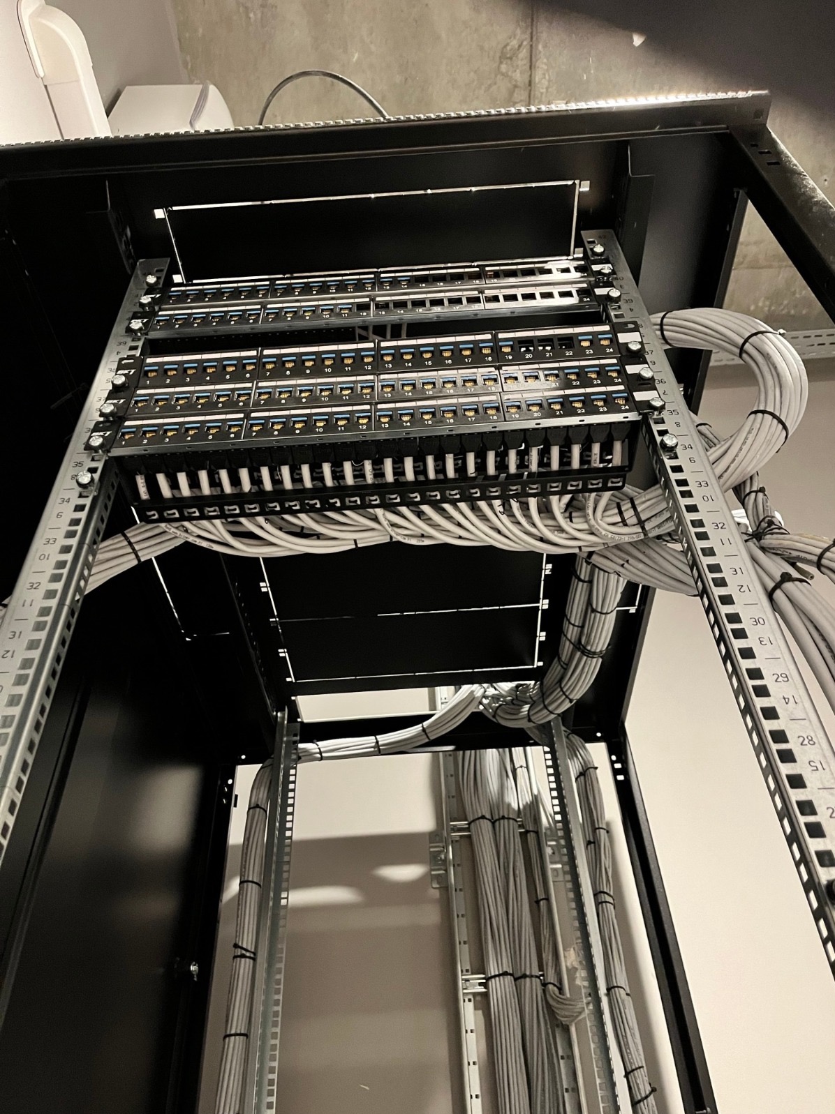 Panel krosowniczy z uporządkowanymi kablami w szafie rack, widok z dołu, ukazujący precyzję i estetykę wykonania instalacji sieciowej.