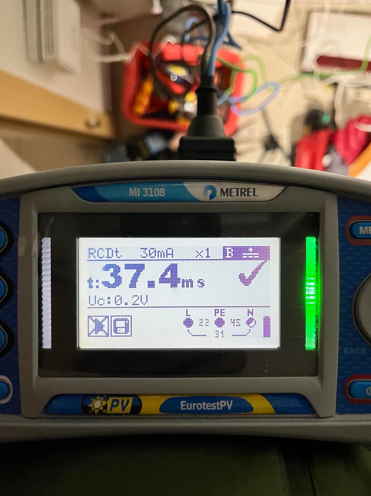 Miernik Metrel MI 3108 EurotestPV z wyświetlonym wynikiem pomiaru RCDt 37.4ms, używany podczas pomiarów elektrycznych. W tle widoczna skrzynka narzędziowa.