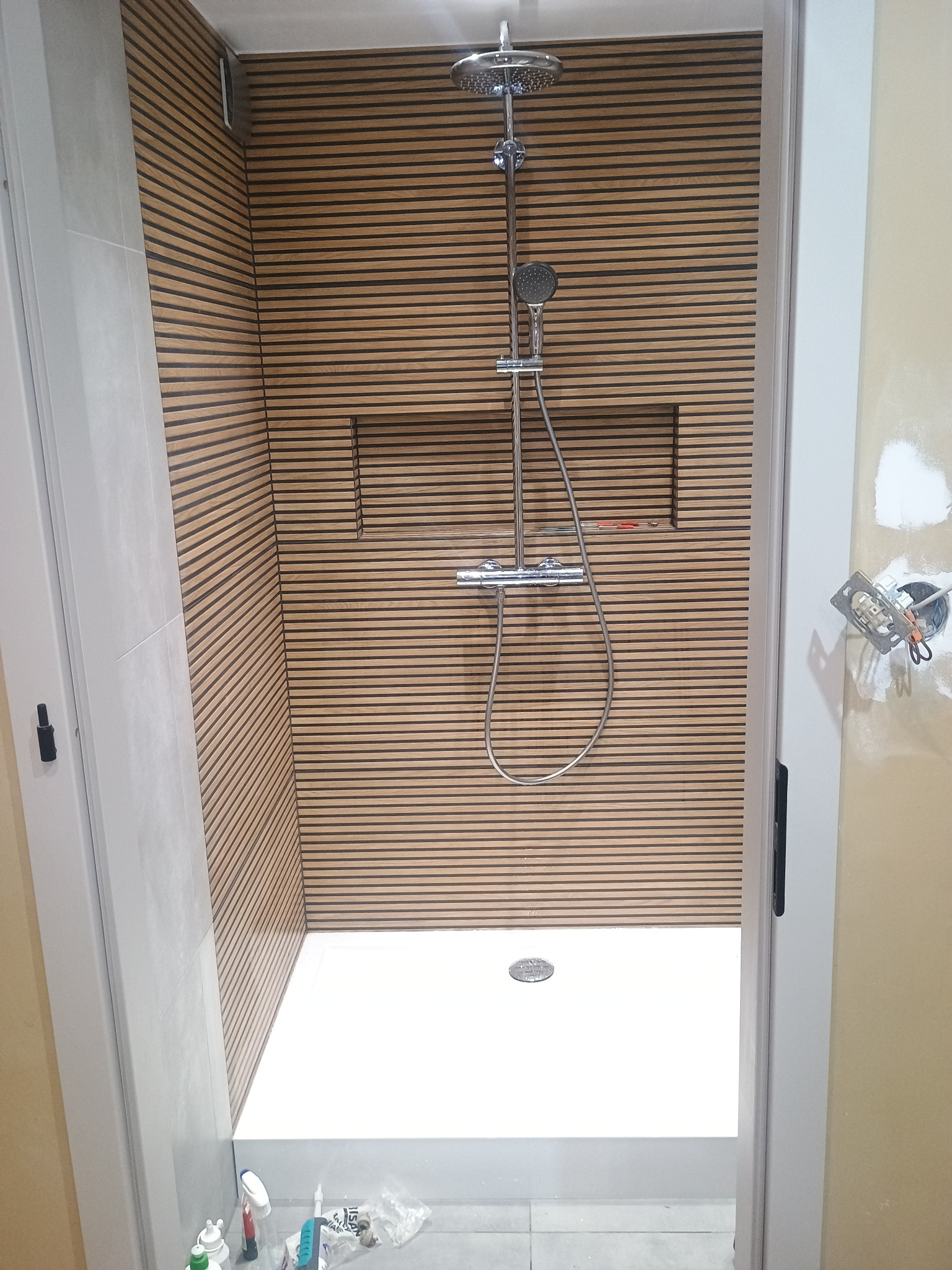 Kabina prysznicowa z drewnianą okładziną w Smolnikach. Nowoczesny design z deszczownicą i wnęką. Widoczne detale wykończenia i instalacja elektryczna.