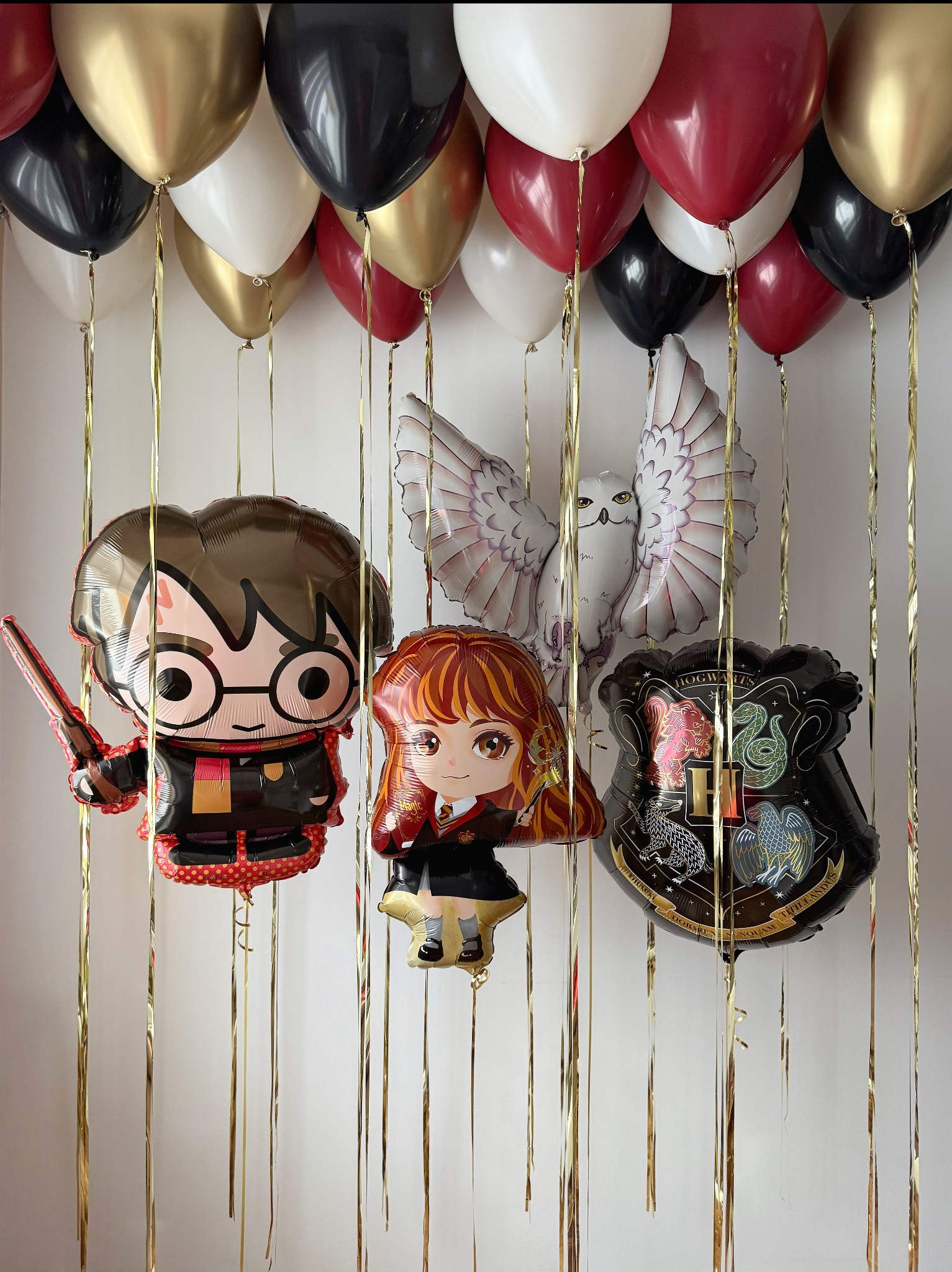 Dekoracja balonowa z motywem Harry'ego Pottera: balony foliowe z postaciami i herbem Hogwartu, balony lateksowe w kolorach czarnym, złotym, białym i bordowym, złote wstążki.