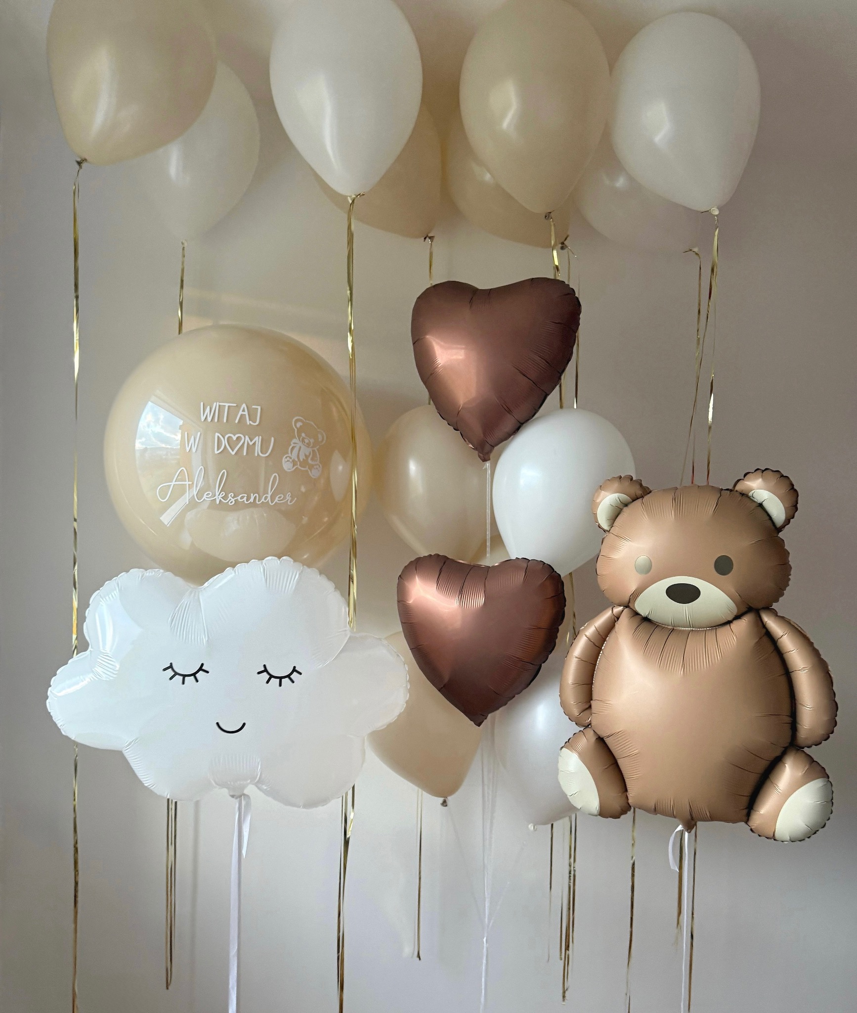 Dekoracja balonowa na powitanie dziecka: beżowe i białe balony, balon w kształcie chmurki z oczami, balon serce i miś. Napis na balonie: Witaj w domu Aleksander.