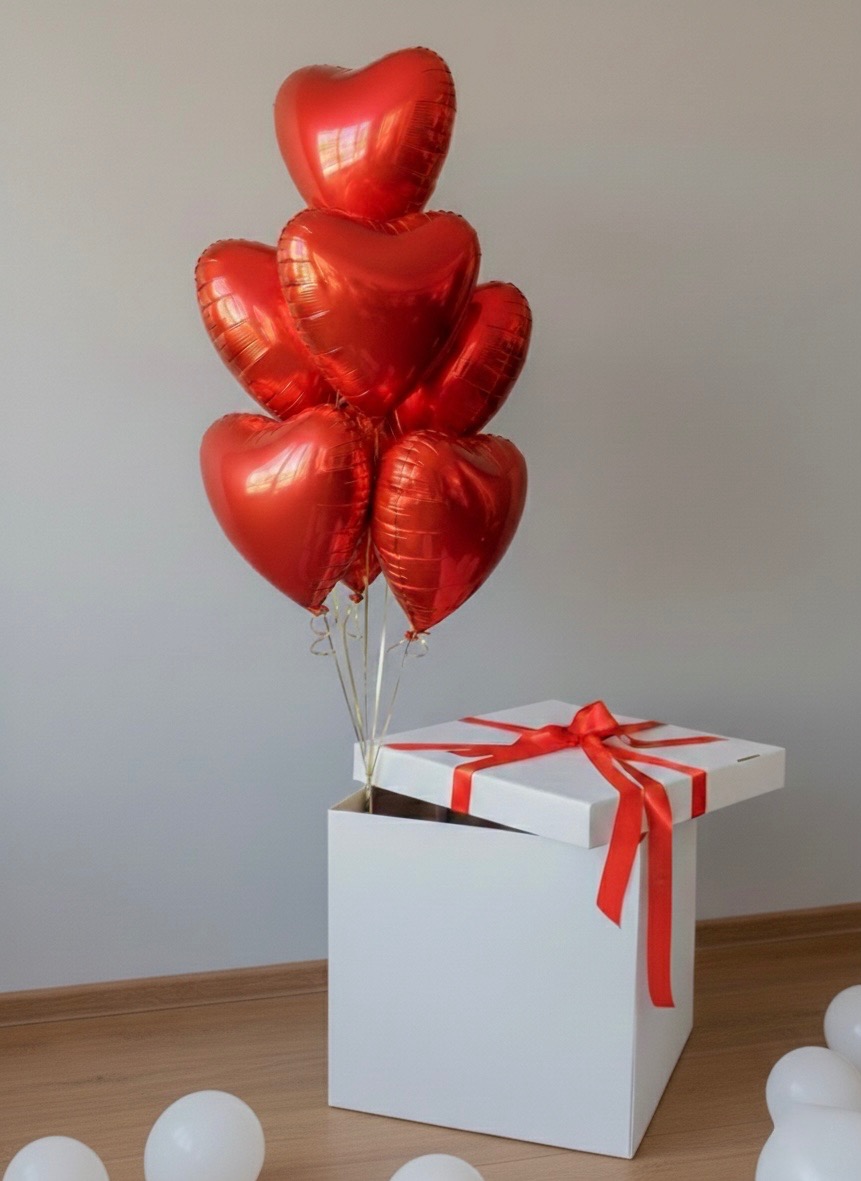 Pudełko z prezentami i czerwonymi balonami w kształcie serc, unoszącymi się z niego. Dekoracja na imprezę okolicznościową, urodziny lub walentynki.