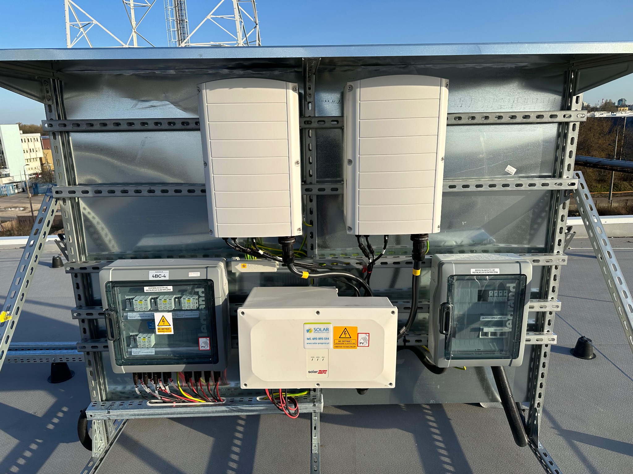 Kompletna instalacja fotowoltaiczna na dachu: inwertery, rozdzielnice AC/DC, okablowanie. Widoczne elementy marki SolarEdge i Legrand. Metalowa konstrukcja wsporcza.