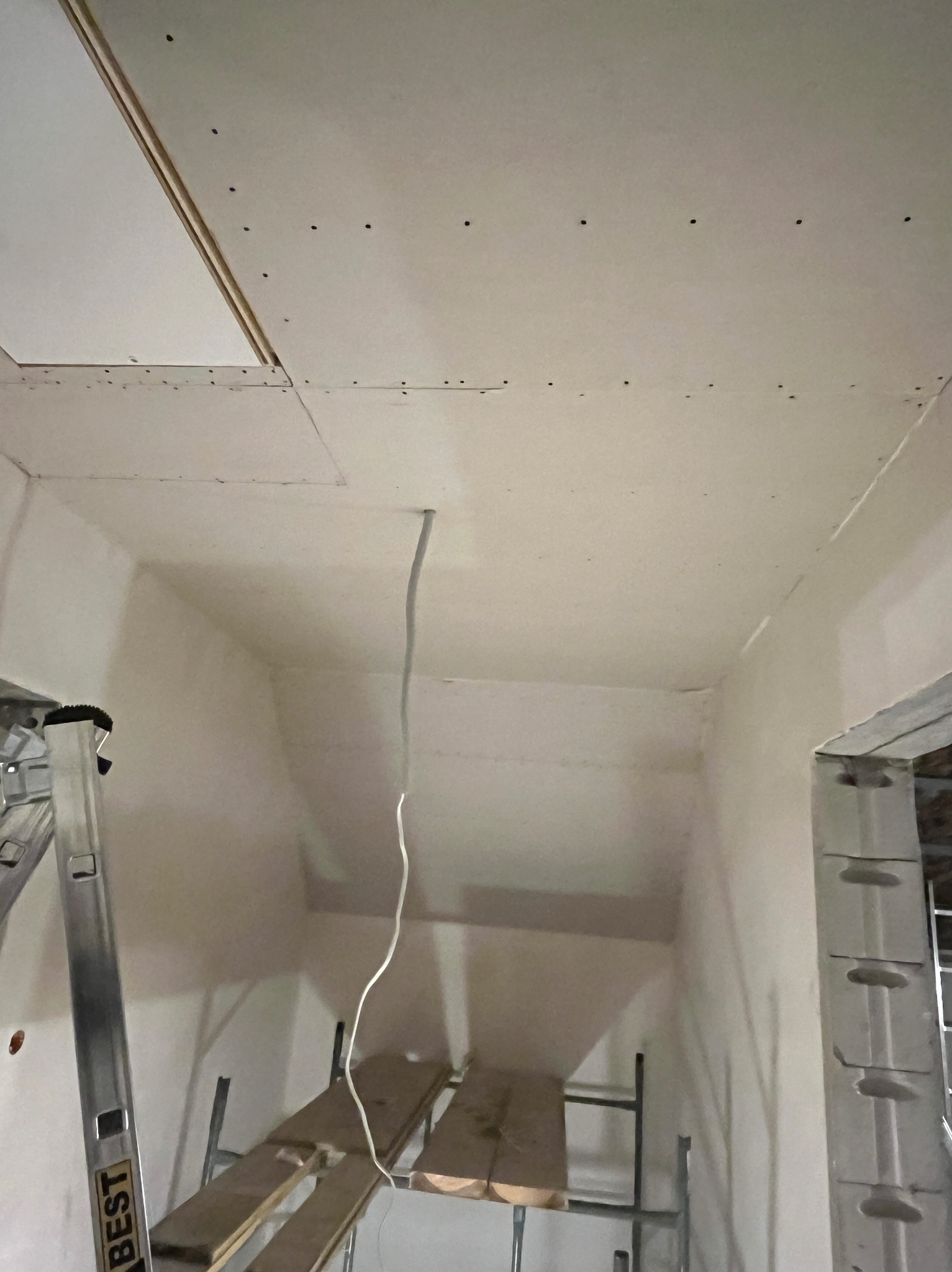 Sufit z płyt gipsowo-kartonowych w trakcie montażu, widoczne kable, rusztowanie i drabina. Ściany przygotowane do dalszych prac wykończeniowych.