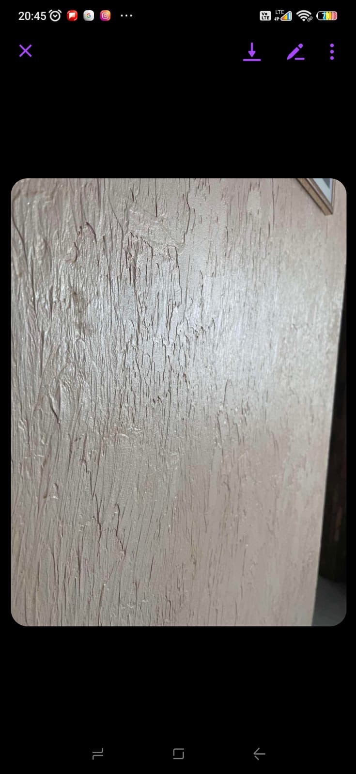 Beżowa ściana z wyraźną, pionową fakturą. Dekoracyjna struktura nałożona równomiernie, tworząca efektowny wzór. Fragment ramy obrazu w prawym górnym rogu.