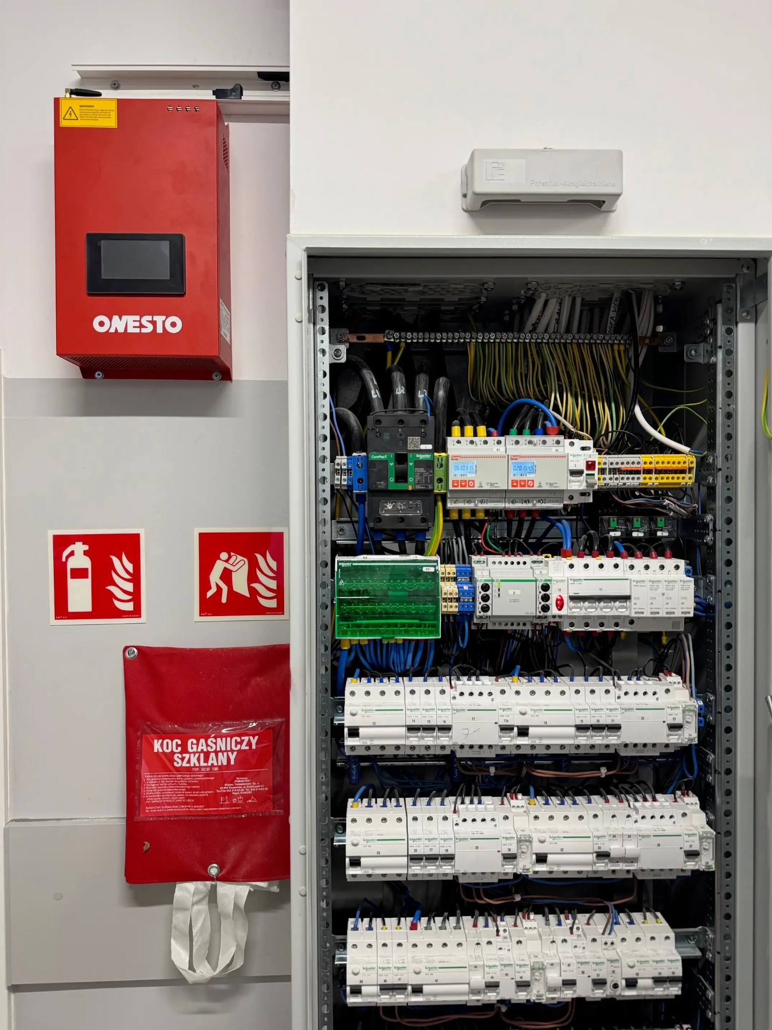 Rozdzielnica elektryczna z zainstalowanymi kompensatorami mocy biernej, widoczne zabezpieczenia przeciwpożarowe: koc gaśniczy i gaśnica.