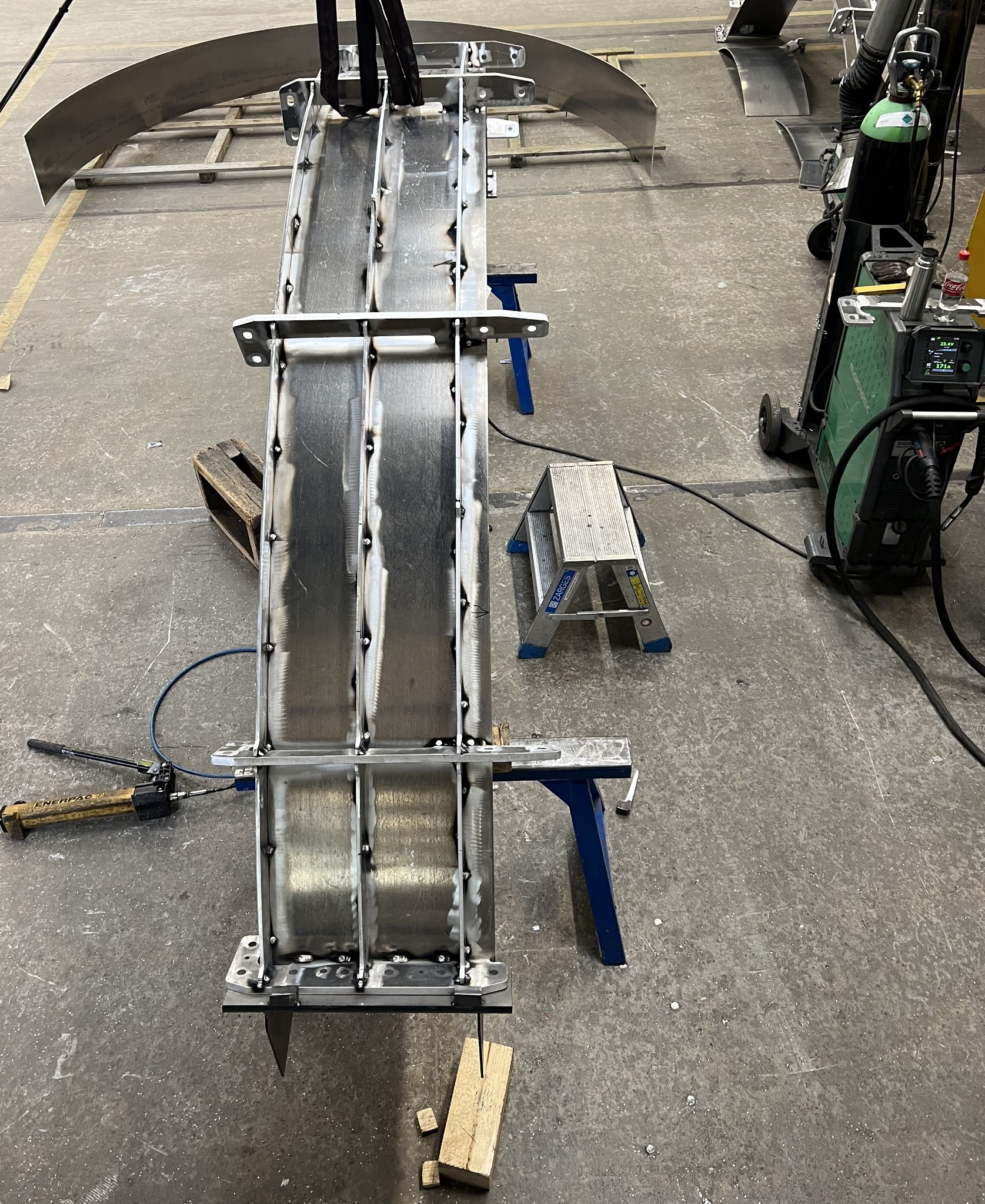 Konstrukcja metalowa w trakcie spawania, widoczne spoiny, narzędzia i elementy montażowe. Detal z blachy nierdzewnej w warsztacie.