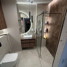 NOW GRES DAMIAN NOWAK - Nowoczesna łazienka po remoncie: kabina prysznicowa typu walk-in, umywalka z szafką z drewnianym fornirem, okrągłe lustro z podświetleniem LED i dekoracyjna ściana z płytek.