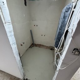 NowGres - Wnętrze łazienki w trakcie remontu: wylana posadzka, ściany przygotowane pod gładzie, widoczne instalacje. Sufit z płyt karton-gips. Metalowy profil przy ścianie.