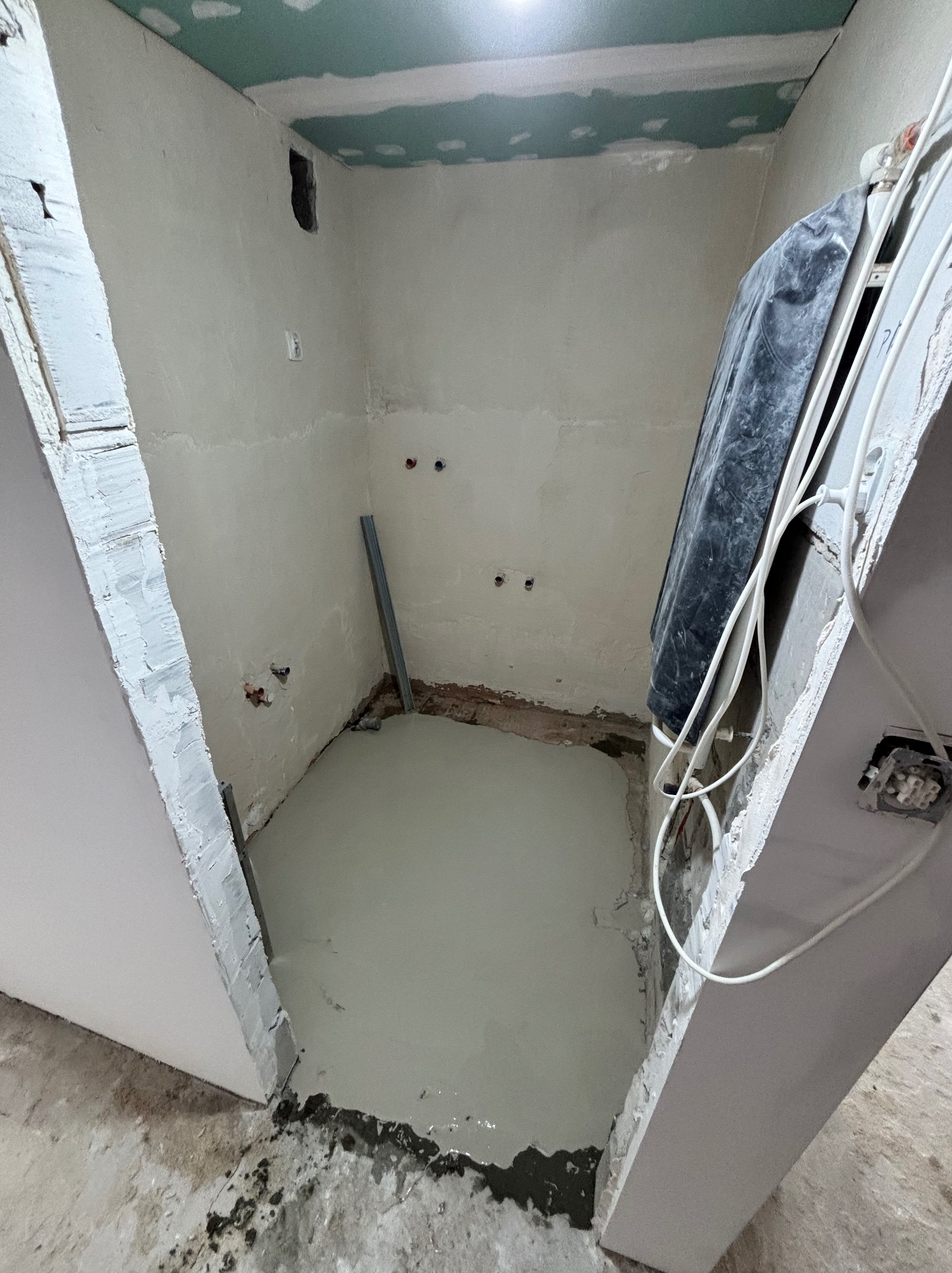 Wnętrze łazienki w trakcie remontu: wylana posadzka, ściany przygotowane pod gładzie, widoczne instalacje. Sufit z płyt karton-gips. Metalowy profil przy ścianie.