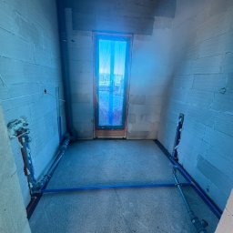 JW SMART SYSTEMS sp. z. o.o - Wnętrze w trakcie instalacji hydraulicznej: widoczne rury PEX w podłodze i przy ścianach z bloczków, okno zabezpieczone folią. Etap prac przed wylewką.