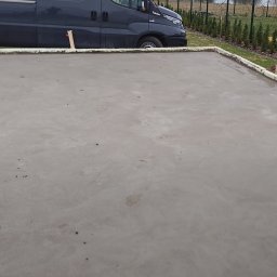 JW SMART SYSTEMS sp. z. o.o - Wylana, świeża płyta fundamentowa z widocznym szalunkiem i zaparkowanym obok samochodem dostawczym. W tle ogrodzenie i zieleń.