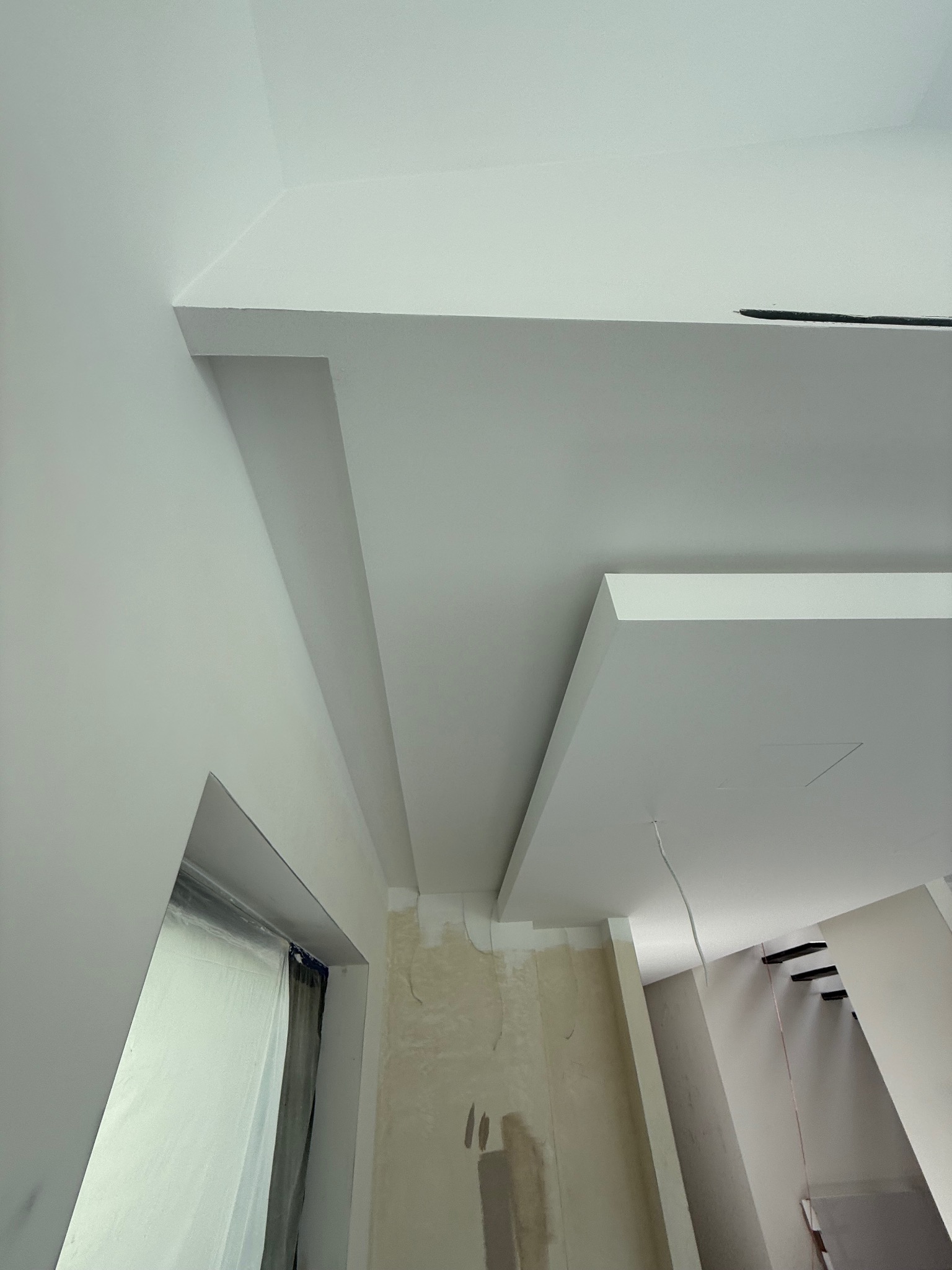 Białe, nowoczesne wykończenie sufitu podwieszanego z oświetleniem punktowym, widok z dołu, fragment ściany z przygotowaniem do malowania.