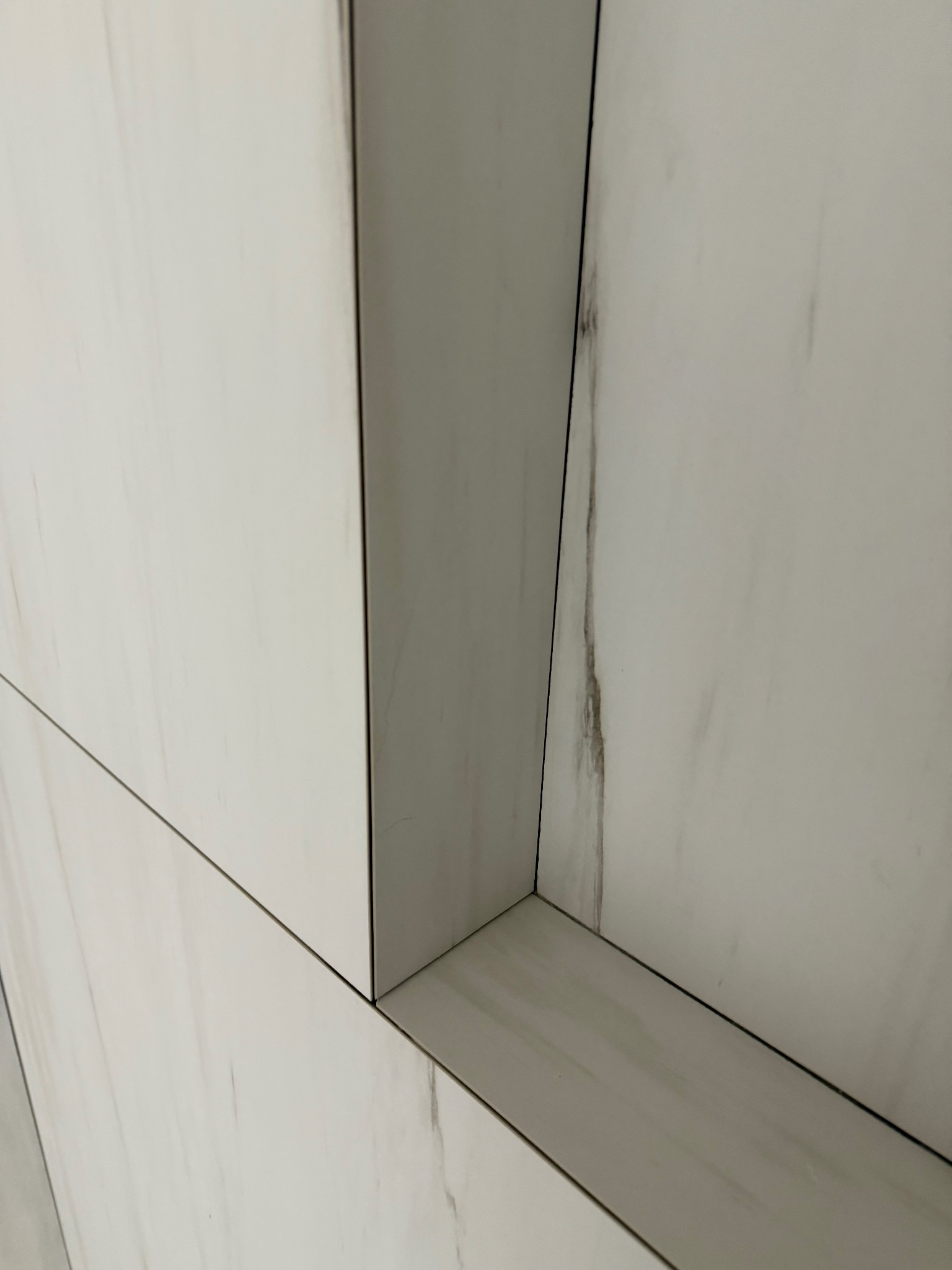 Detal narożnika wykończonego białymi płytkami imitującymi marmur. Widoczne precyzyjne łączenia i subtelny wzór żyłkowania. Minimalistyczny design.