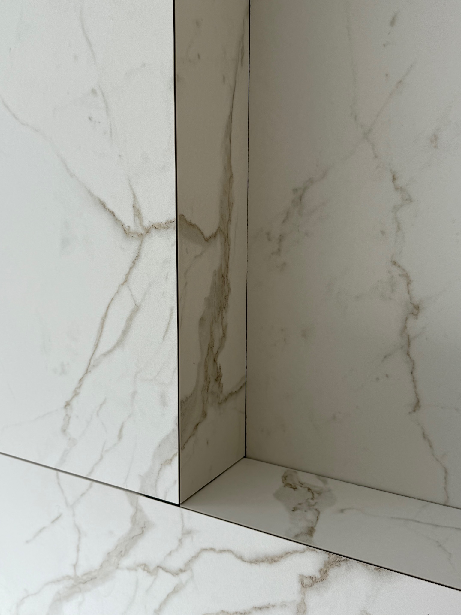 Połączenie trzech płaszczyzn płytek imitujących marmur, tworzących narożnik. Widoczne delikatne żyłki w odcieniach brązu. Minimalistyczny design.