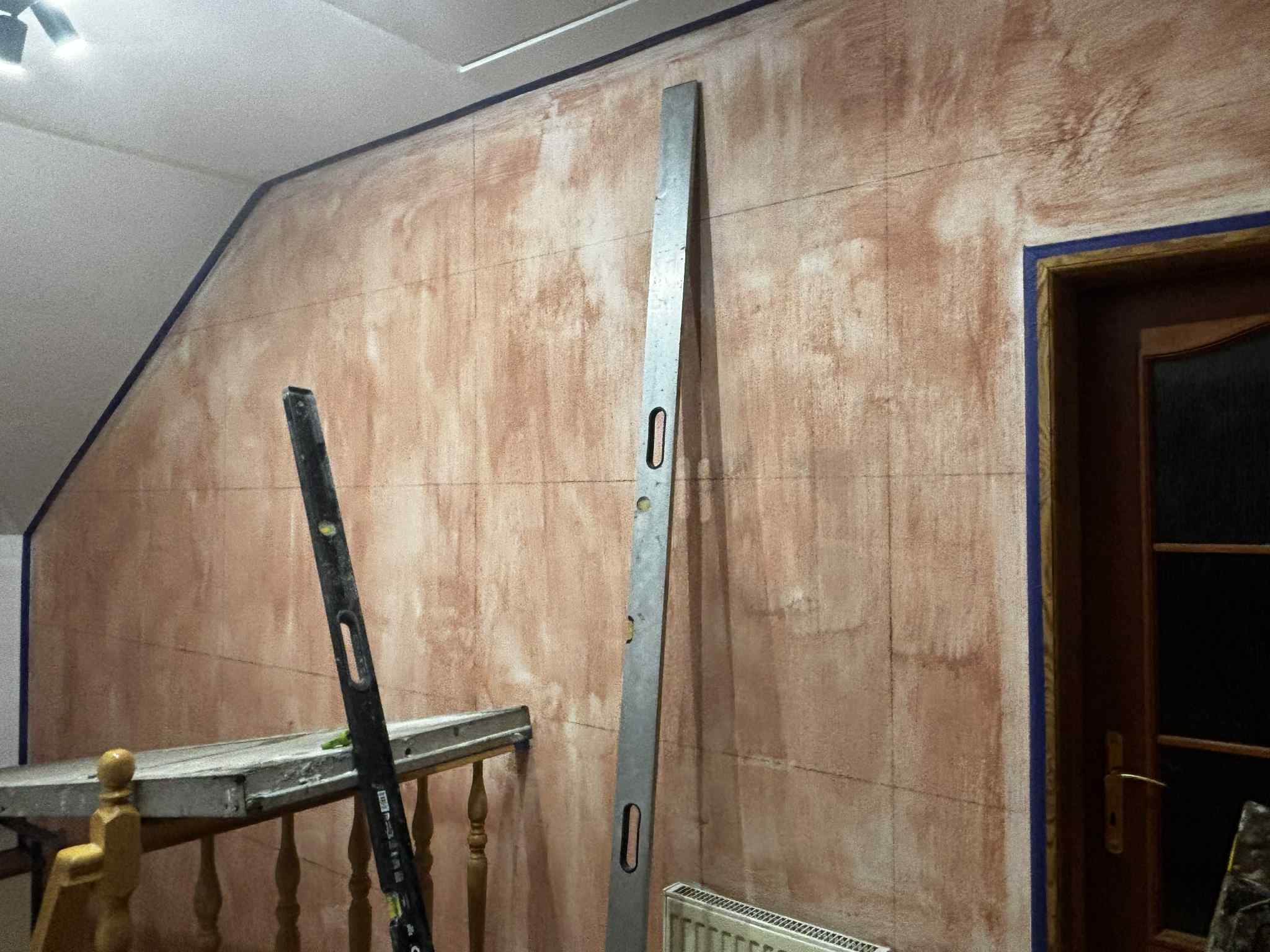 Ściana po nałożeniu warstwy podkładowej, z widocznymi liniami pomocniczymi i poziomnicami. Przygotowanie do dalszych prac wykończeniowych wnętrza.