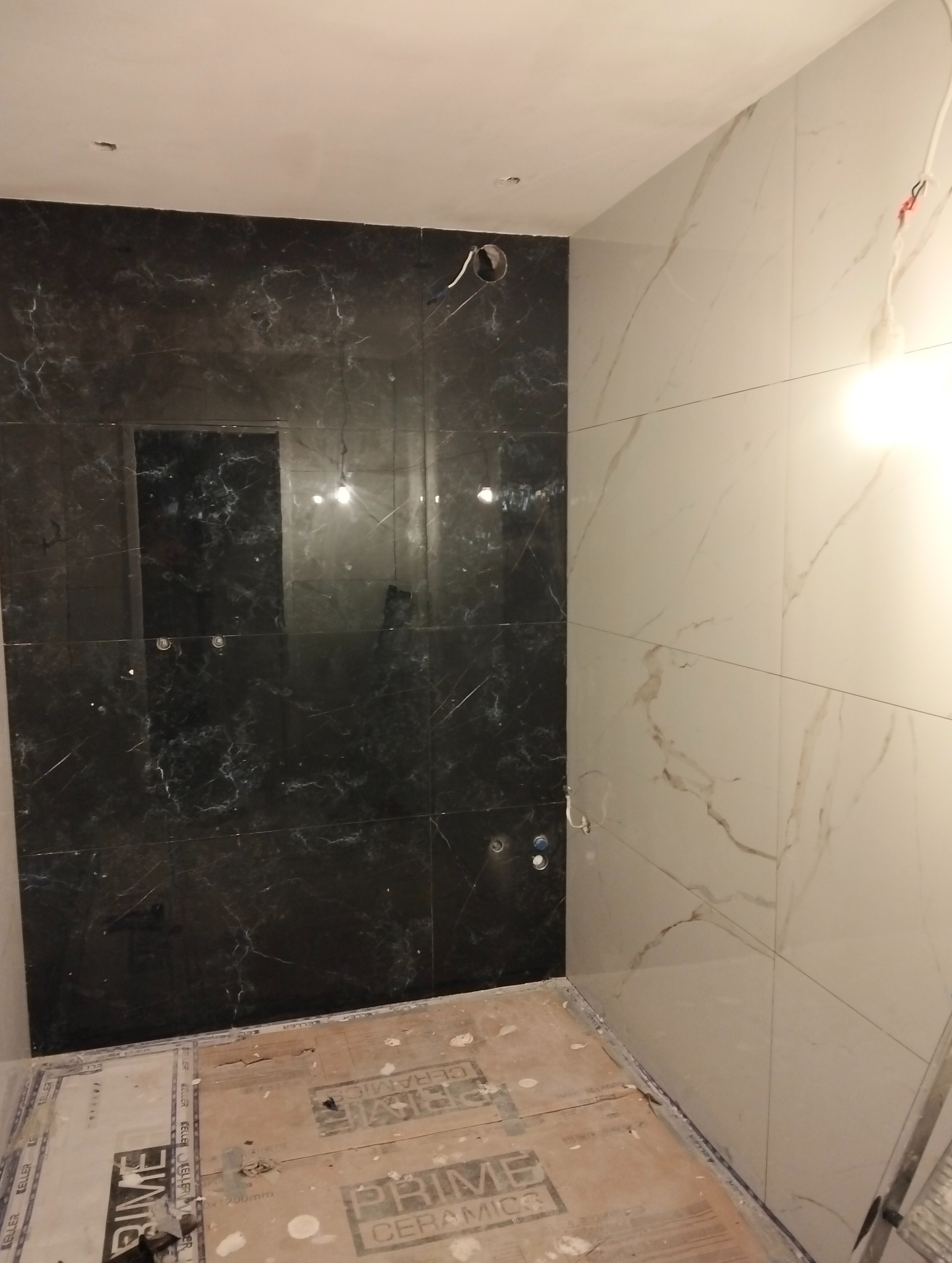 Łazienka w trakcie wykańczania: ściany wyłożone czarnymi i białymi płytkami imitującymi marmur, widoczne otwory na armaturę, podłoga przygotowana pod dalsze prace.