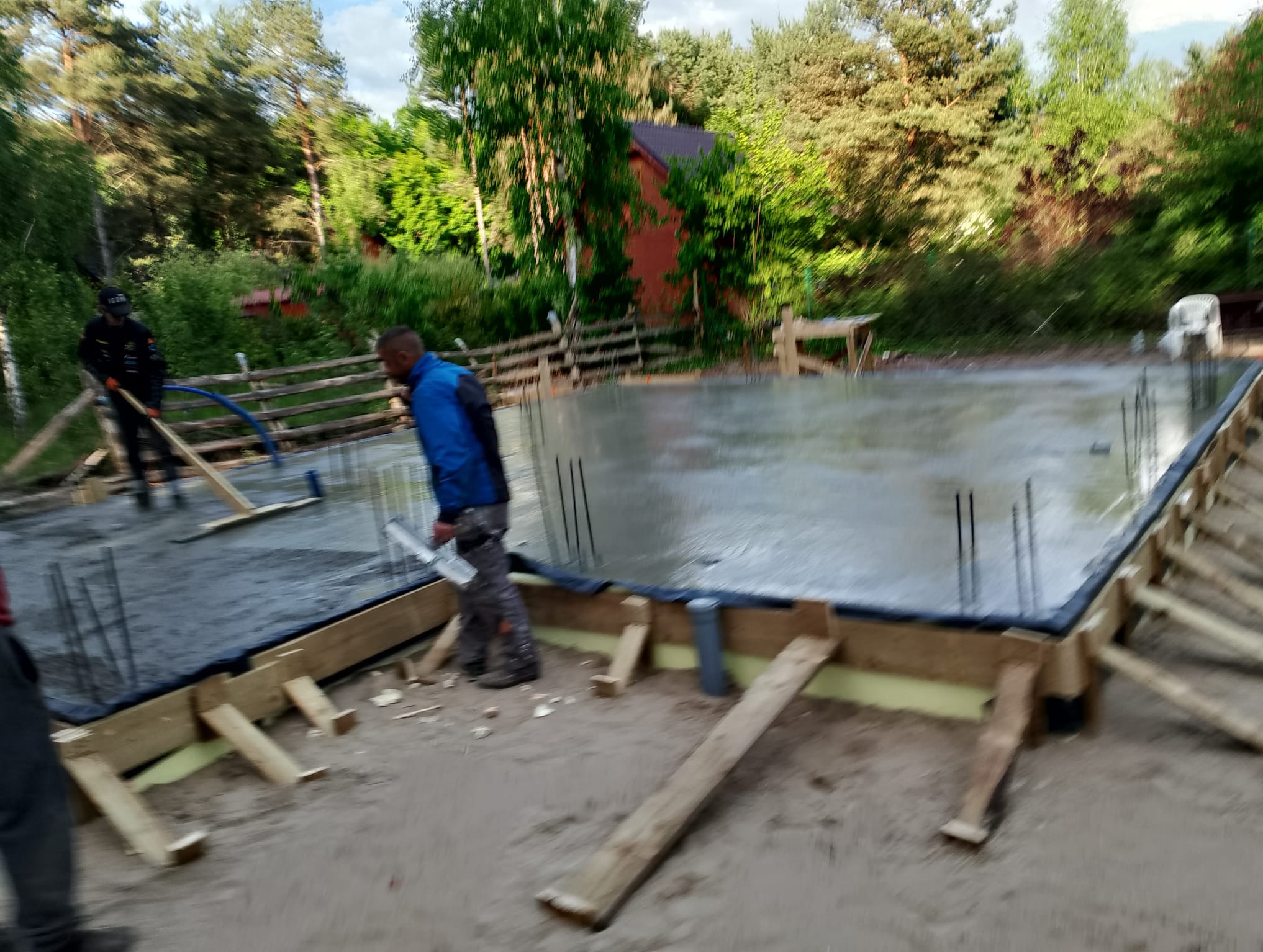 Wylewka fundamentów pod dom jednorodzinny w Warszawie. Widoczne zbrojenia i szalunki. Prace budowlane w toku, teren zalesiony w tle.