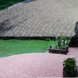 WAHOsoftwash Miękkie Mycie Elewacji - Mycie Kostki Brukowej - Zapraszam Do Galerii Realizacji - Kostka brukowa po czyszczeniu: górna połowa brudna, dolna czysta, ukazująca efekt usługi. Widoczny trawnik i dekoracyjna ławka w tle. Układ radialny kostki.