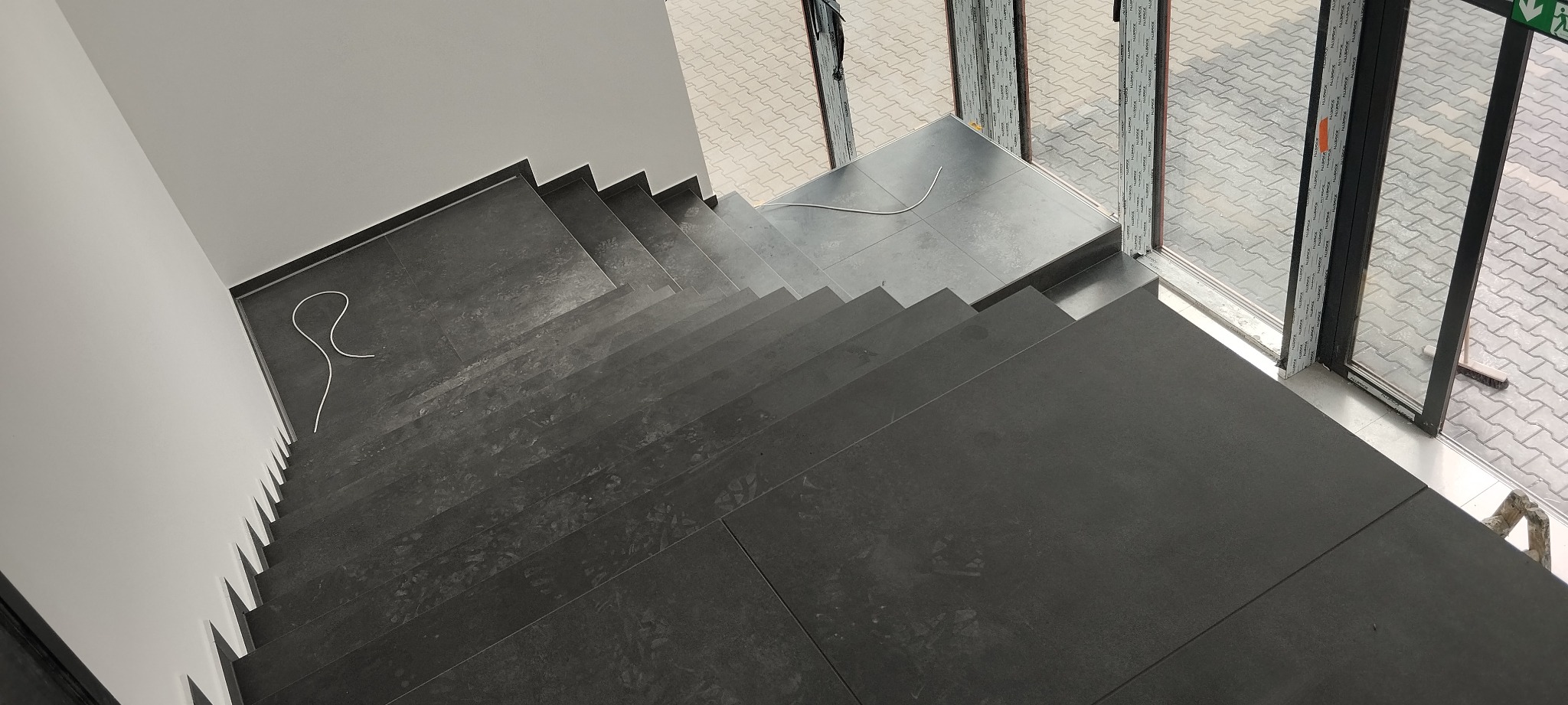 Wykończone schody z ciemnych płytek, widok z góry, z białymi ścianami i oknami w Sarnach. Widoczny kabel na schodach.