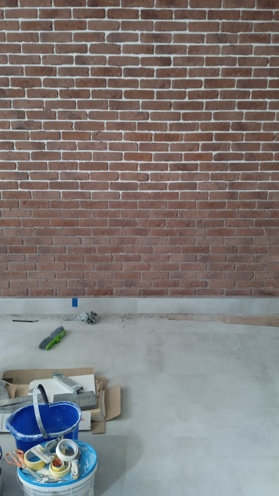 Ściana z cegły klinkierowej z białymi fugami, widok z dołu, z narzędziami i materiałami budowlanymi na podłodze. Układanie cegieł na ścianie.