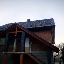Usługi ciesielsko dekarskie - Dom z nowym, ciemnym dachem i rynnami w Brzyskiej Woli. Widoczny fragment elewacji z cegły i drewniane elementy konstrukcyjne.