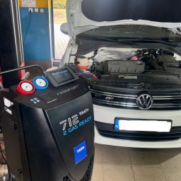 Mechanika Samochodowa SZYNALIK Damian Szynalik - Biały samochód z otwartą maską w warsztacie, podłączony do czarnego urządzenia Texa do serwisowania klimatyzacji. Widoczne manometry i ekran dotykowy.