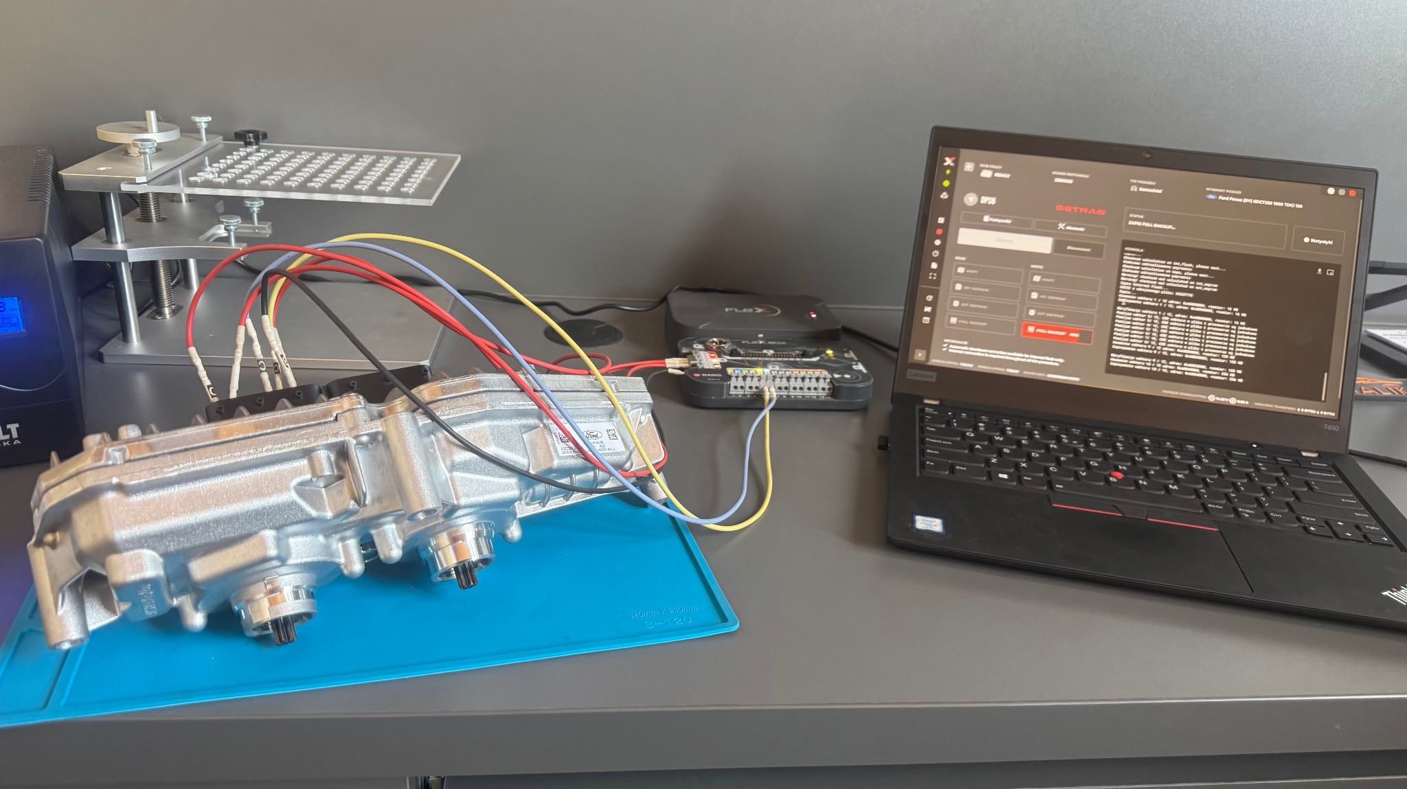 Skrzynia biegów podłączona przewodami do urządzenia diagnostycznego i laptopa z uruchomionym oprogramowaniem. Diagnostyka i naprawa automatycznej skrzyni biegów.