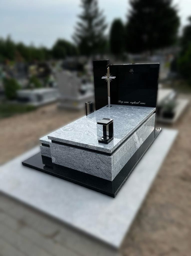 Granitowy nagrobek z krzyżem w Kleczewie. Szara płyta z czarnym panelem i inskrypcją. Widok na cmentarz, nagrobek dwupoziomowy, nowoczesny styl.