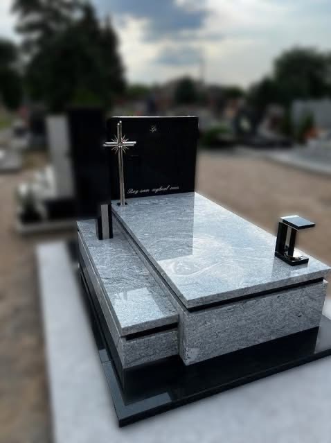 Granitowy nagrobek z krzyżem i inskrypcją, jasnoszary blat z ciemnymi żyłkami, czarna podstawa i tablica, widok z boku, cmentarne tło.