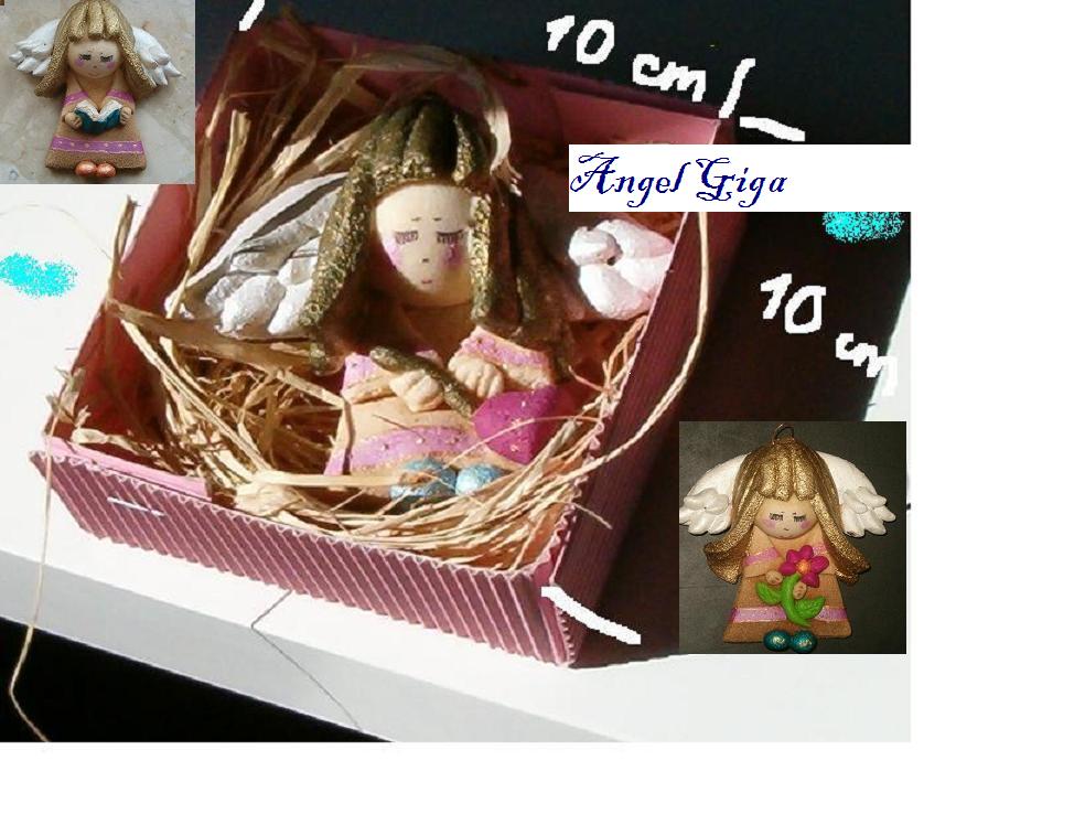 Ręcznie robiona figurka anioła z gliny, umieszczona w tekturowym pudełku wypełnionym siankiem; dodatkowe figurki aniołów w tle.