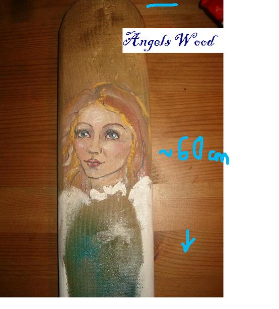 Ręcznie malowana postać anioła na desce z jasnego drewna, z widoczną fakturą drewna i niedoskonałościami malowania, umieszczona na tle drewnianego blatu.