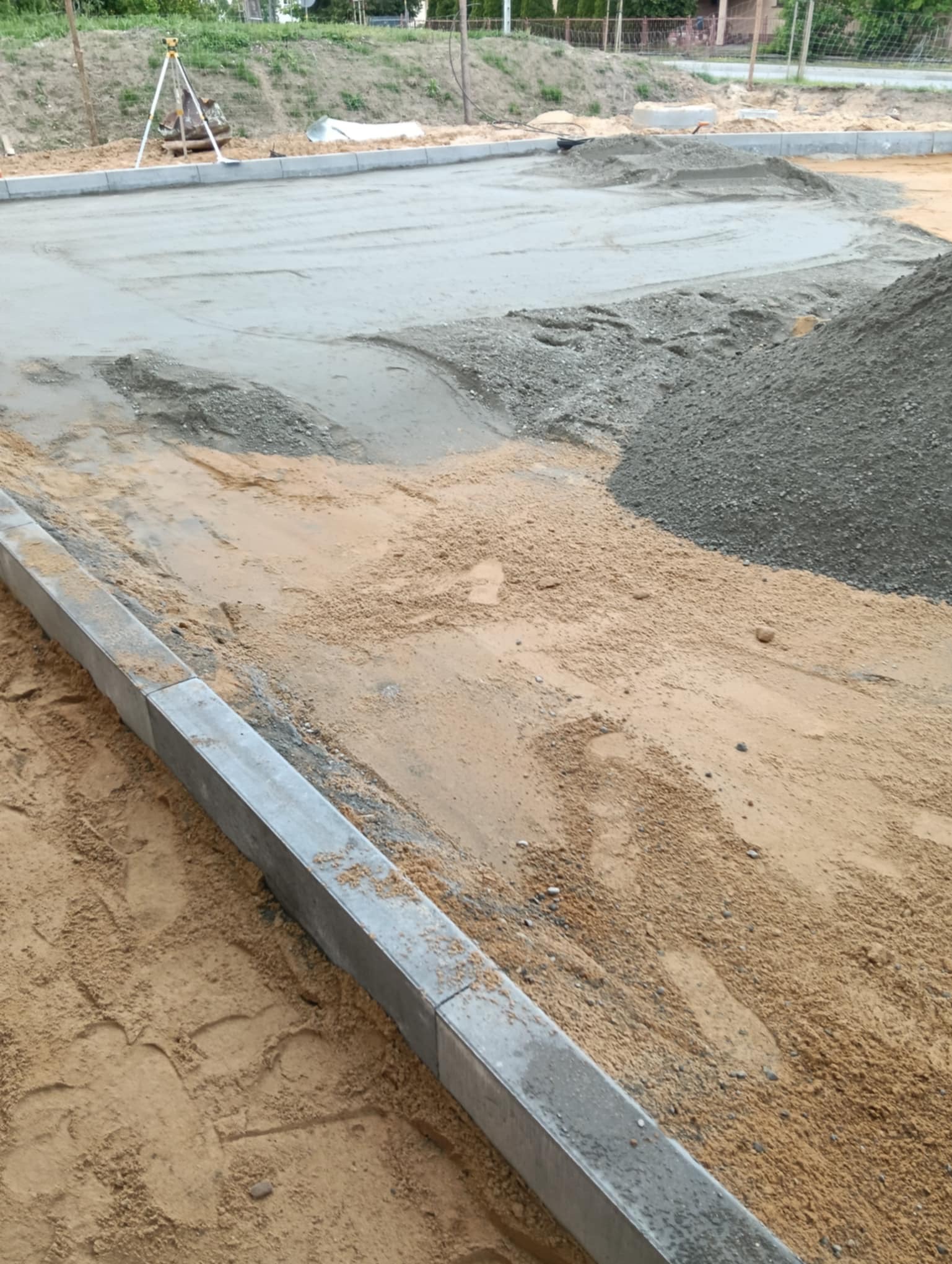 Przygotowanie podłoża pod kostkę brukową: wyrównany piasek, podsypka cementowo-piaskowa, ustawione obrzeża. W tle niwelator laserowy.