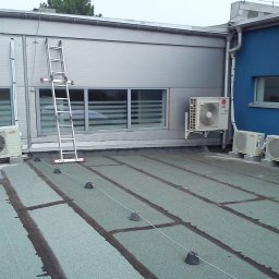 Bartosz - Instalacja klimatyzacji na dachu budynku z drabiny. Widoczne jednostki zewnętrzne klimatyzatorów LG i Lennox, kable, elementy montażowe i fragment elewacji.