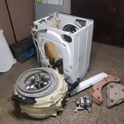Bartosz - Rozłożona pralka automatyczna z widocznymi elementami: bęben, obudowa, silnik i inne części na podłodze. Widoczne ślady użytkowania i demontażu.