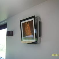 Klimatyzator ścienny z obrazem w ramce, nietypowa instalacja w Myszkowie. Biała ściana, widoczny fragment lampy. Narożne ujęcie, klimatyzacja wkomponowana w wystrój.