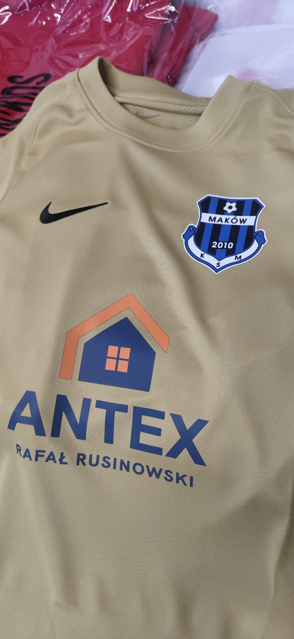 Beżowa koszulka sportowa z nadrukiem logo firmy ANTEX i herbu klubu sportowego Maków, widoczny znak Nike. Detal odzieży z personalizowanym wzorem.