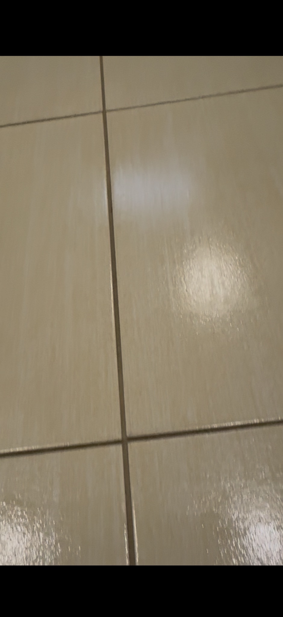 Błyszcząca, beżowa podłoga z płytek ceramicznych po umyciu, widoczne fugi. Perspektywa z dołu, podkreślająca czystość i odbicie światła.