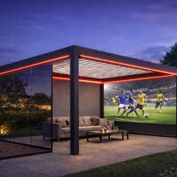 Adrian Durak - Nowoczesna, czarna pergola z oświetleniem LED i szklaną ścianą, wyposażona w sofę i stolik kawowy. W tle widoczny mecz piłki nożnej na ekranie.