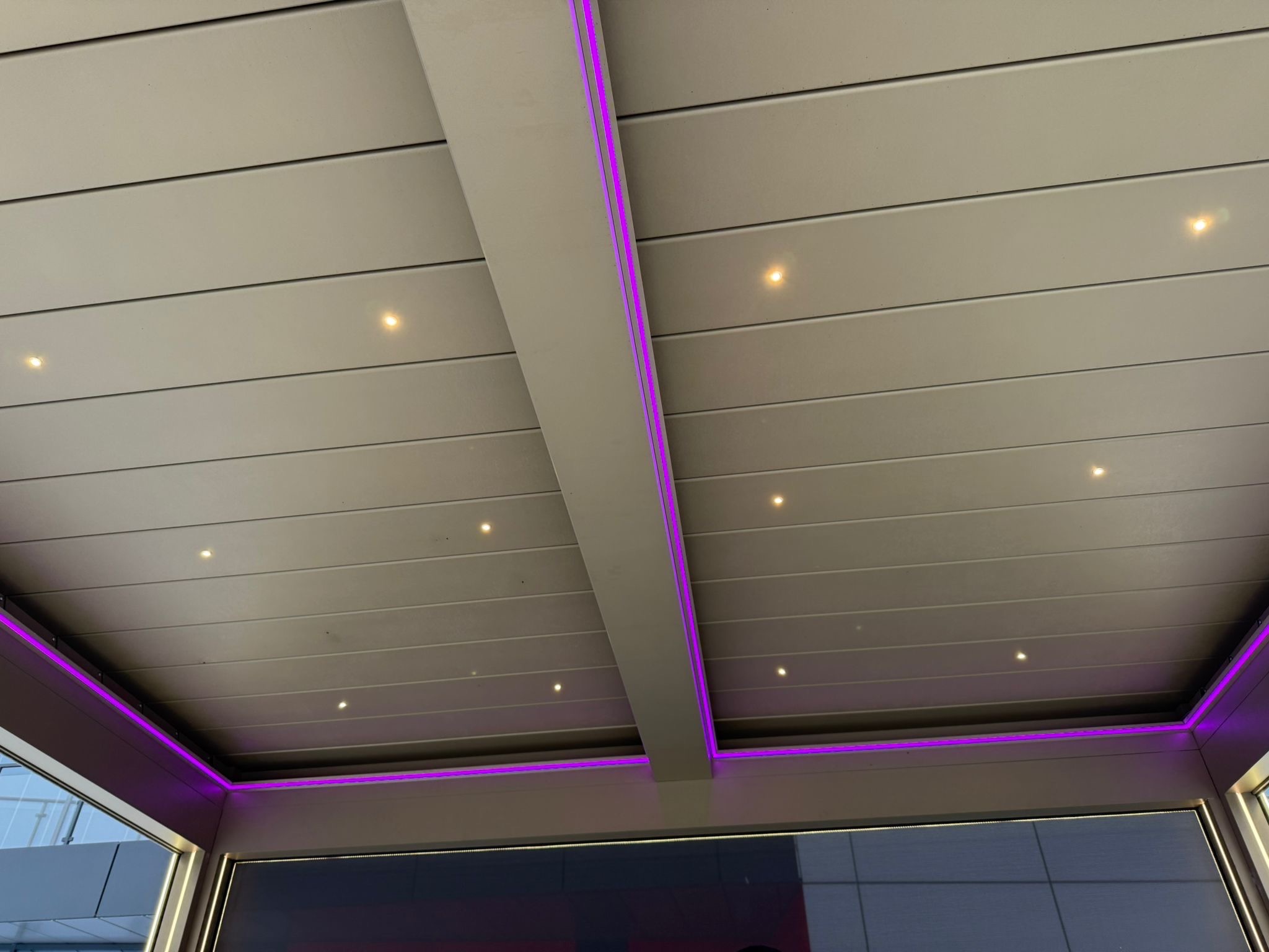 Nowoczesna pergola z metalu z oświetleniem LED w kolorze fioletowym i punktowymi lampkami. Widok z dołu, podkreślający design i detale wykończenia.