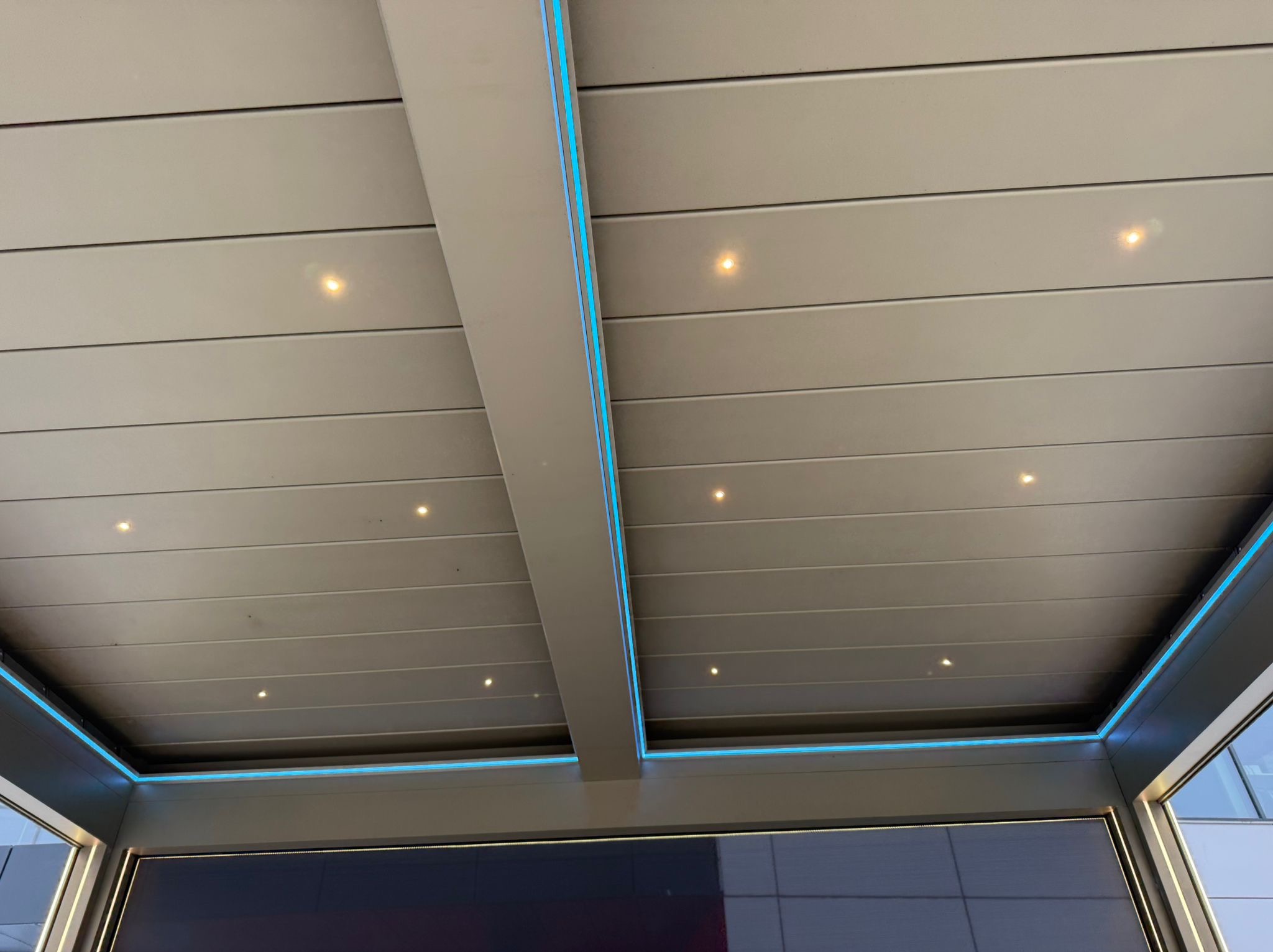 Nowoczesna pergola z metalu z oświetleniem LED, widok od dołu. Subtelne punkty świetlne w suficie i niebieskie paski LED podkreślają konstrukcję. Minimalistyczny design.