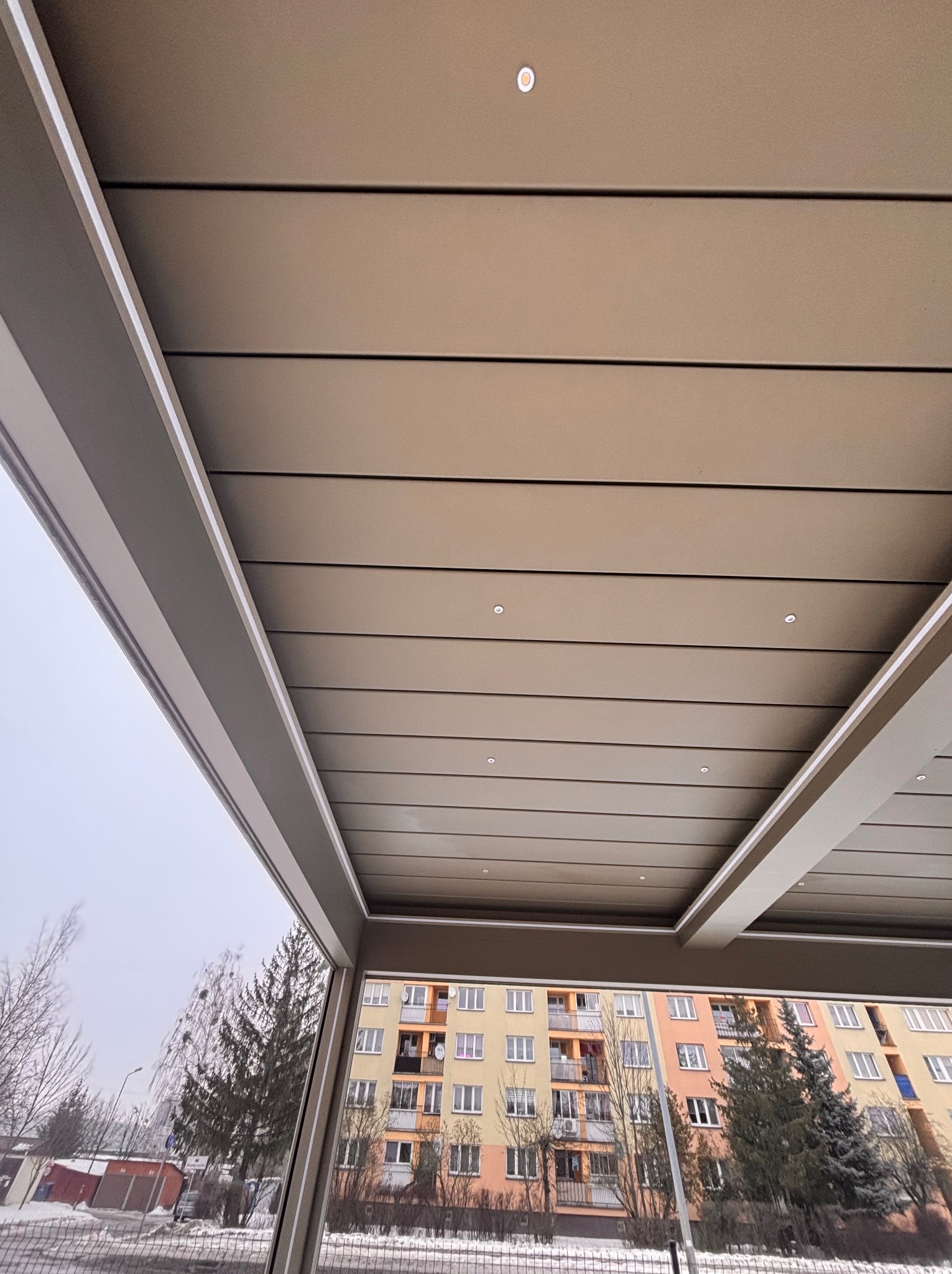 Nowoczesna zabudowa balkonu z oświetleniem LED w Gózdek, widok z dołu na sufit i otoczenie budynku mieszkalnego.