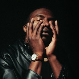 fredieme.photo - Alfred Wiśniewski - Portret mężczyzny w skórzanej kurtce, z dłońmi na twarzy, w dramatycznym oświetleniu. Widoczny zegarek na nadgarstku i kolczyk w uchu. Ciemne tło.